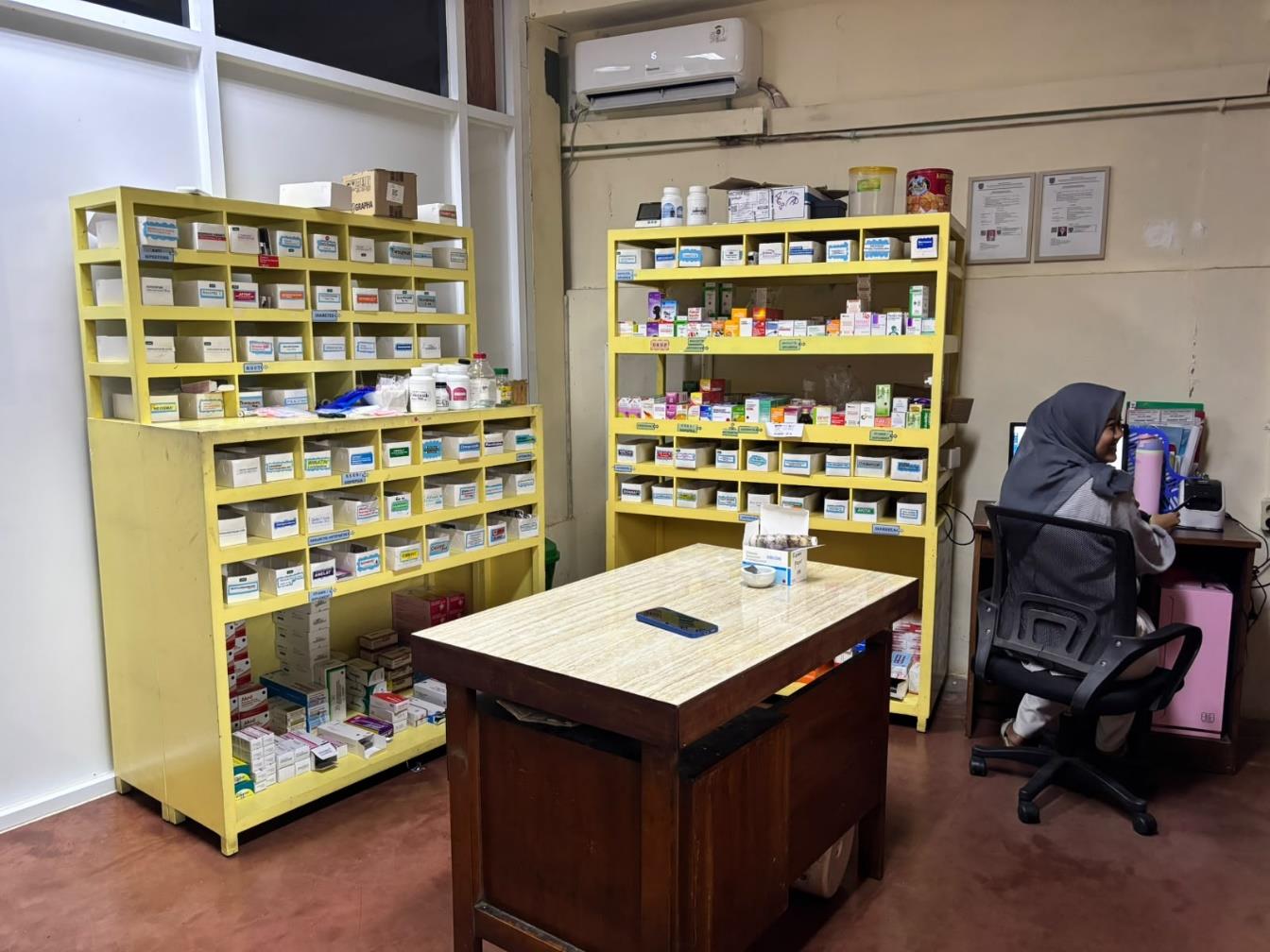 Petugas di ruang farmasi di samping rak obat berwarna kuning