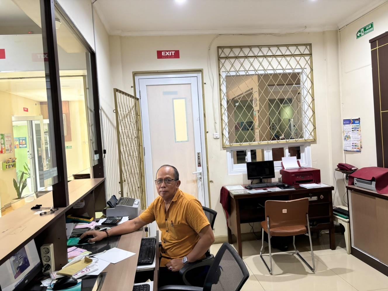 Petugas di meja pendaftaran dengan komputer dan loket kaca